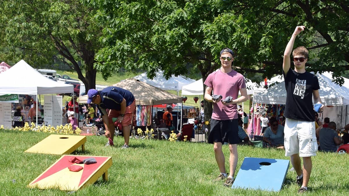 Two people playing cornhole on painted boards set up on a grass lawn at a summer festival